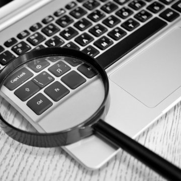 us search online background check service review magnifying glass over laptop keyboard